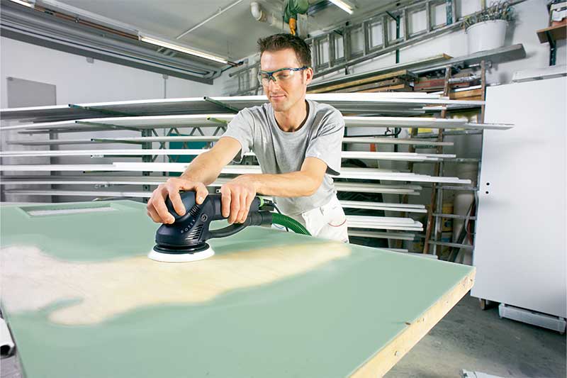 Ein Mann schleift eine grün lackierte Oberfläche